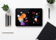 A clean, minimalist workspace with a modern tablet displaying colorful handwritten notes surrounded by office supplies.