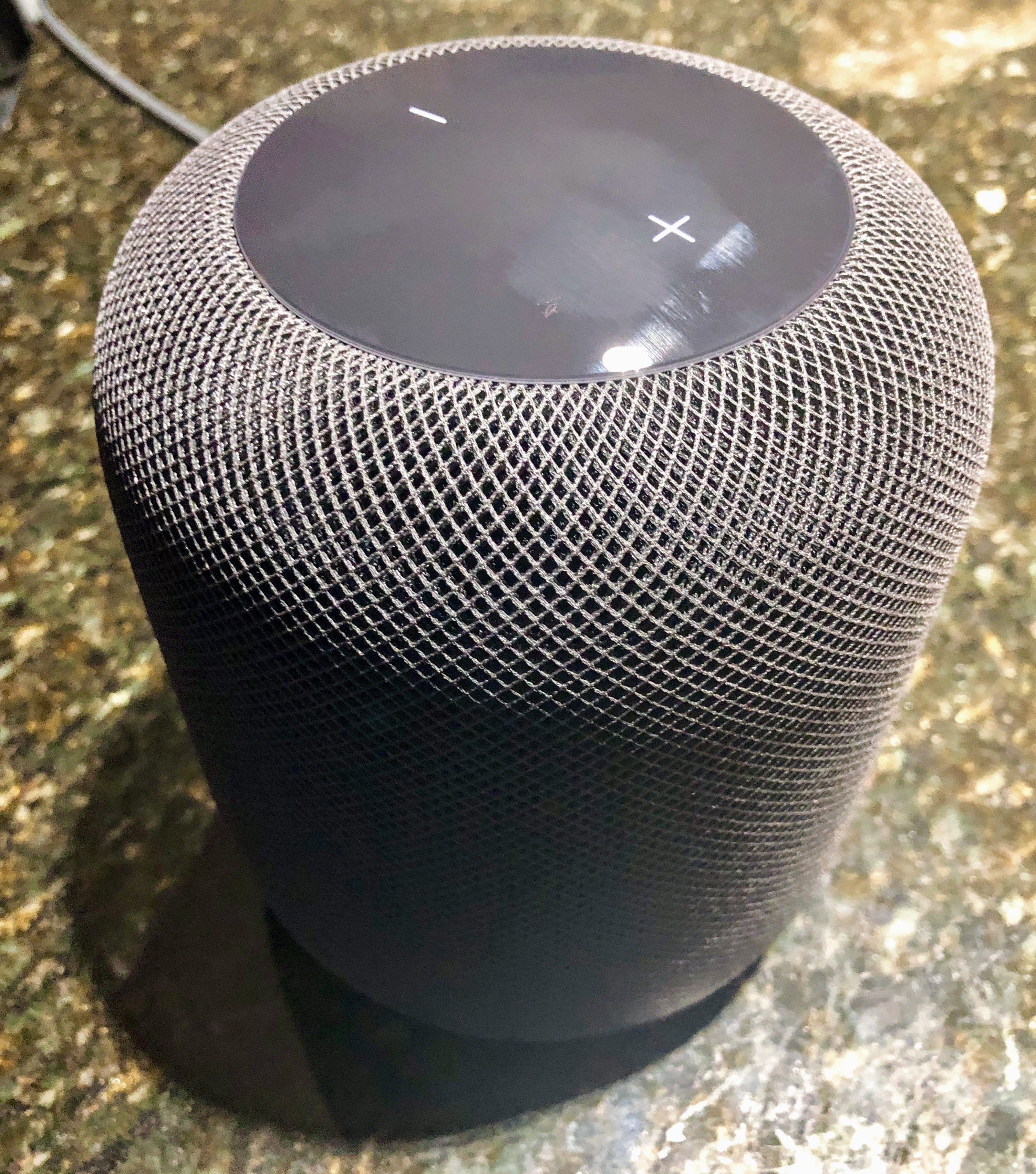 A modern smart speaker with a woven mesh exterior on a surface.