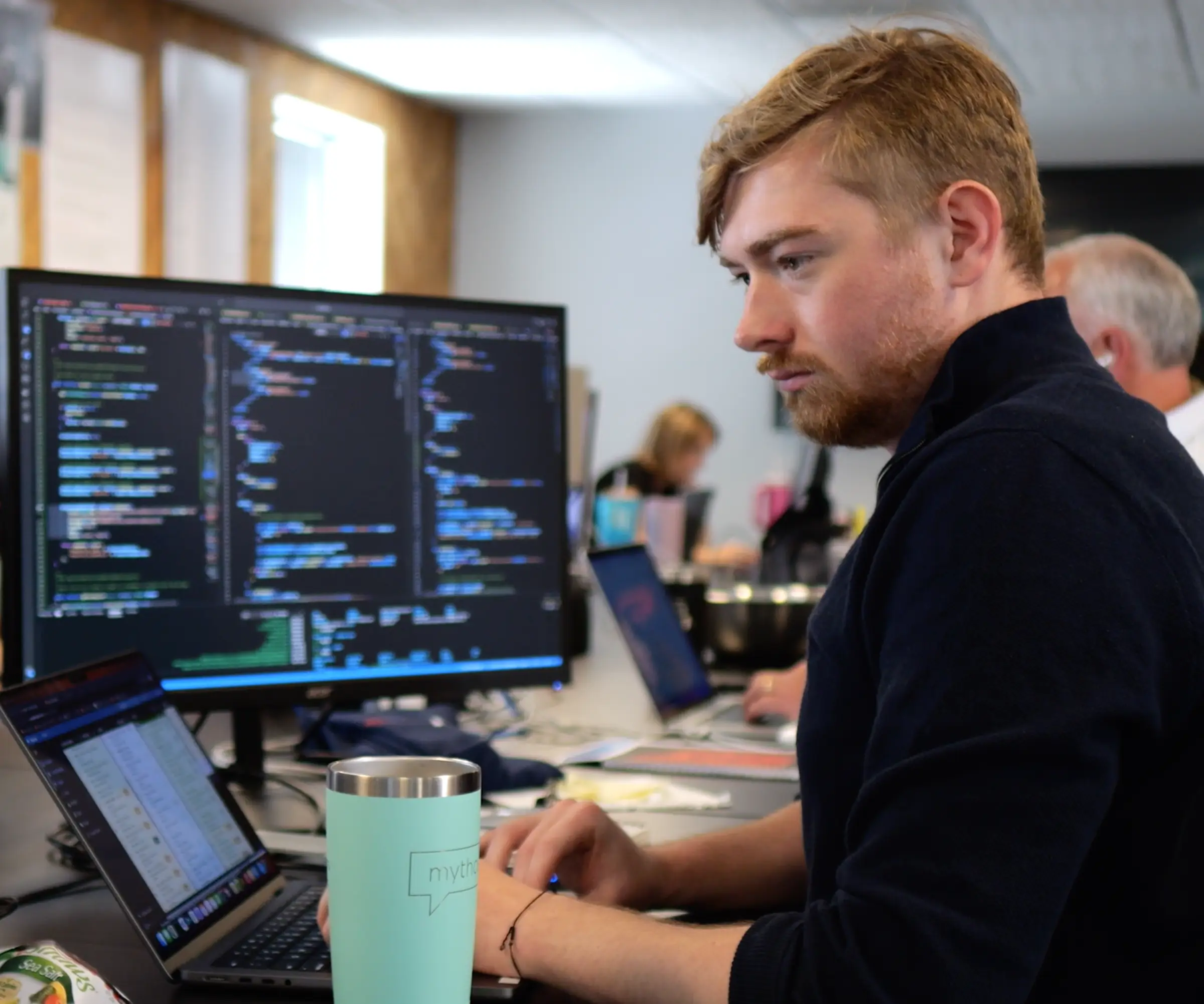 A focused individual coding on dual screens in an office.