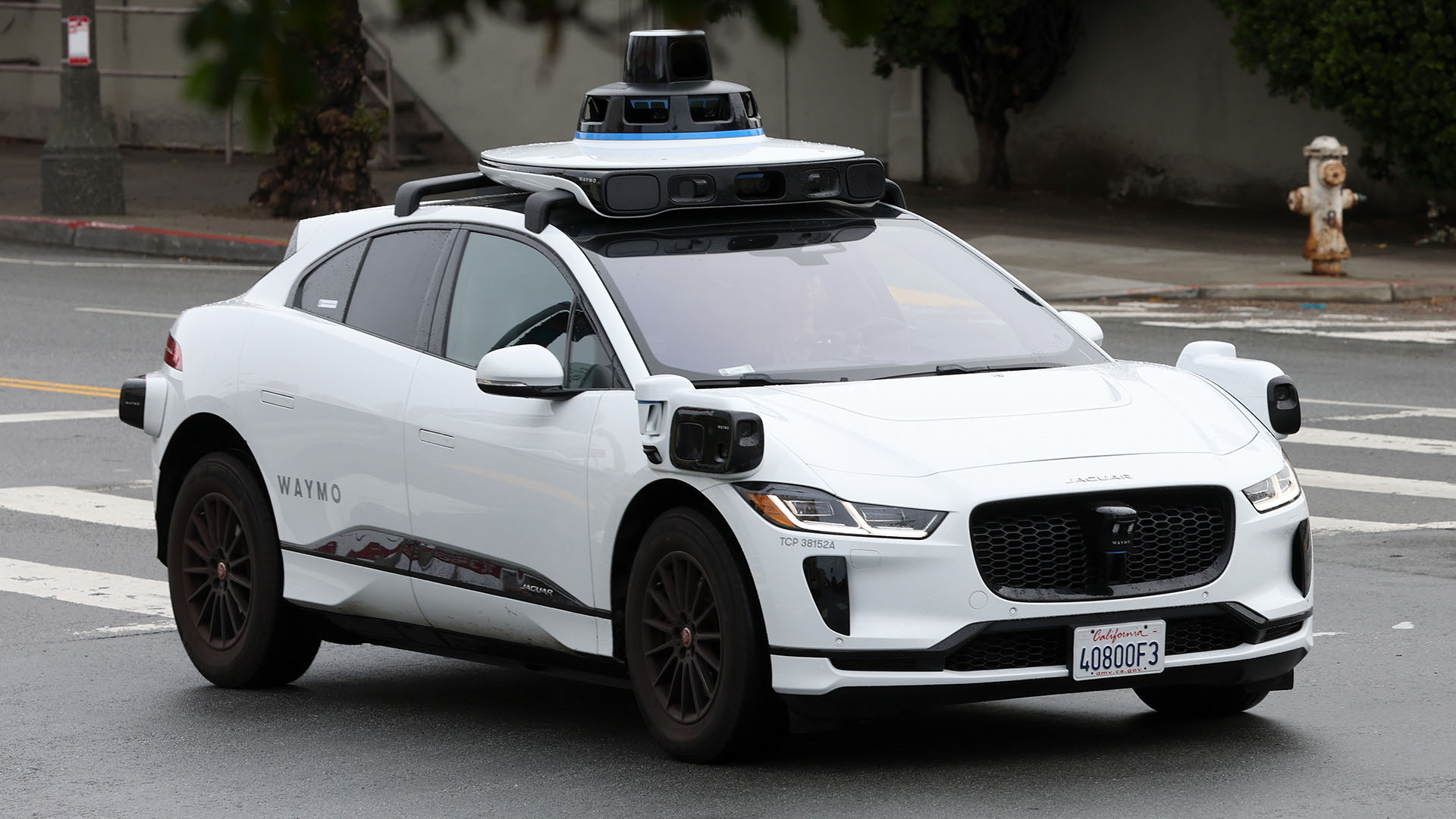 A white autonomous vehicle with sensors driving in a city.