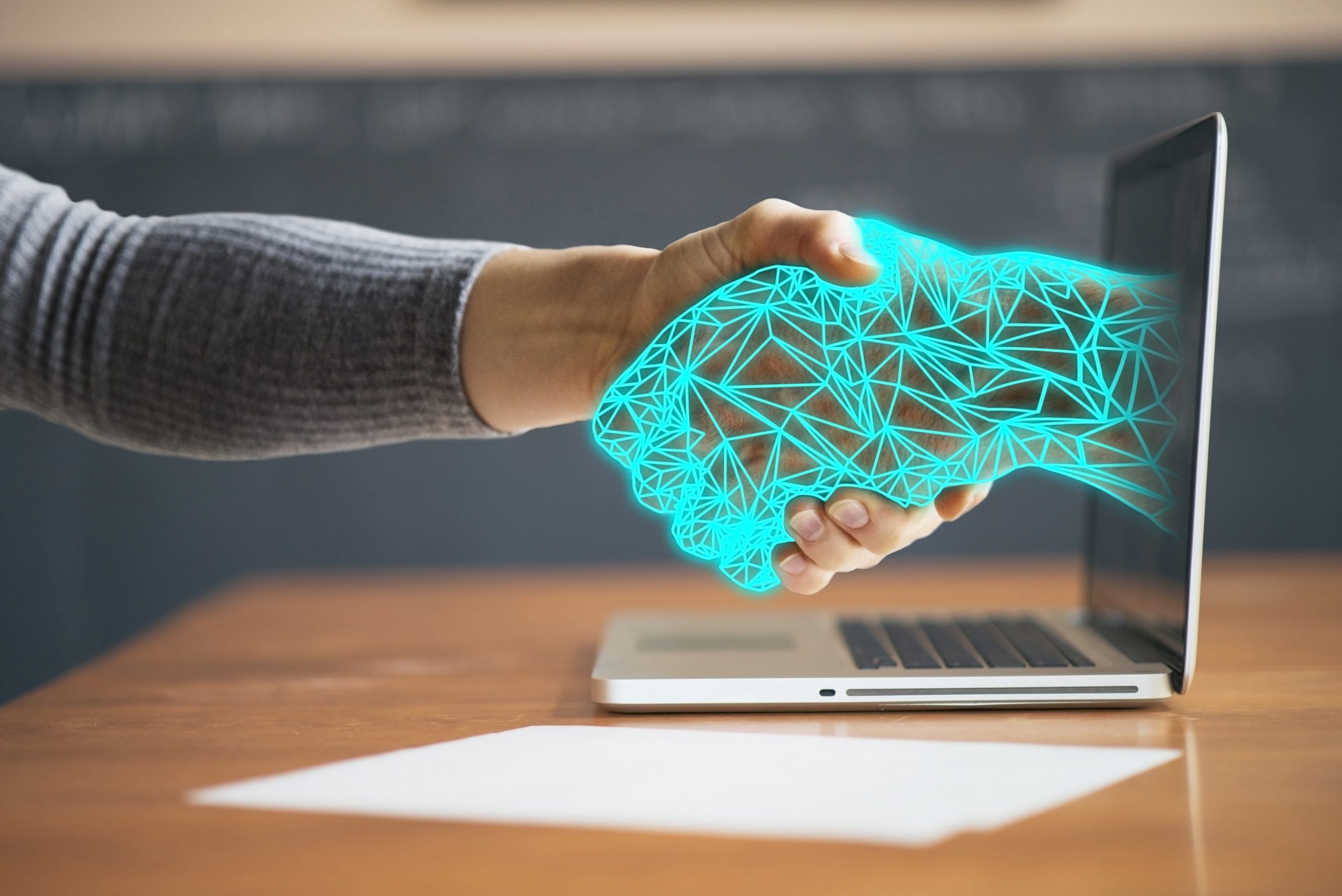 A hand emerging from a laptop screen for a digital handshake