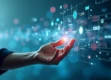 A human hand reaching out to touch a softly glowing digital interface with holographic elements in a minimalist setting.