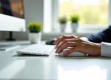 A sleek, modern workspace with a white desk and laptop, featuring a hand using a wireless mouse in soft natural light.