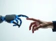 A sleek robotic hand reaching out to touch a human hand against a clean white background, illuminated by soft blue light.
